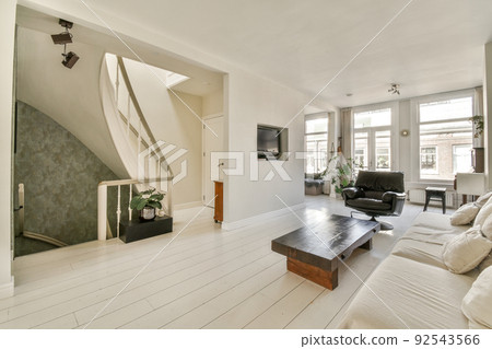 Stylish interior design of living room with light furniture and soft comfy couch and carpet and with TV on cabinet in modern apartment with open kitchen and white walls and column. 92543566