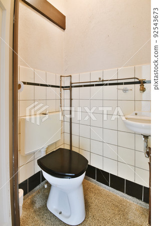 Wall hung toilet and small sink in corner in lavatory room with beige tile 92543673