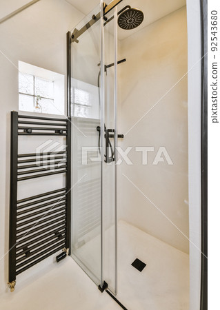 Shower faucets attached to tiled wall near glass partition and ornamental curtail in washroom at home Shower faucets attached to tiled wall near glass partition and ornamental curtail in washroom at home 92543680