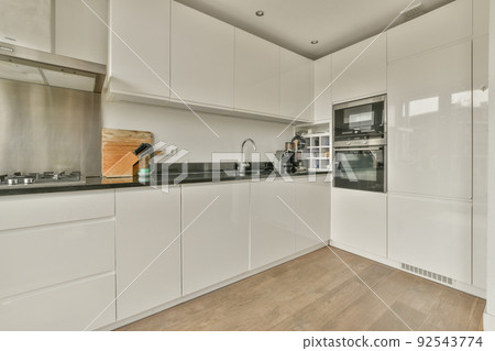 Fragment of interior of light narrow home kitchen with minimalist style white furniture with sink and stove 92543774