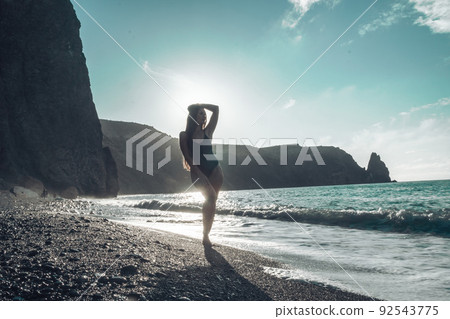 Selective focus. Happy carefree sensual woman with long hair in black swimwear posing at sunset beach. Silhouette of young beautiful playful positive woman outdoor. Summer vacation and trip concept Selective focus. Happy carefree sensual woman with long hair in black swimwear posing at sunset beach. Silhouette of young beautiful playful positive woman outdoor. Summer vacation and trip concept 92543775