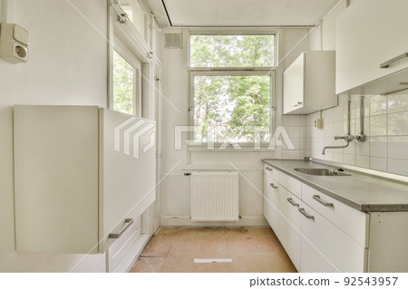 Interior of minimalist style kitchen with simple cupboards and modern appliances in light apartment Interior of minimalist style kitchen with simple cupboards and modern appliances in light apartment 92543957