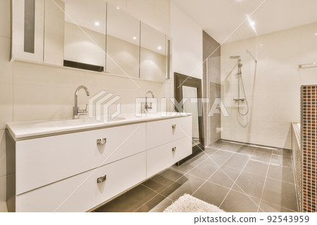 Sinks with mirrors and shower box with glass door in modern bathroom with white tiled walls Sinks with mirrors and shower box with glass door in modern bathroom with white tiled walls 92543959