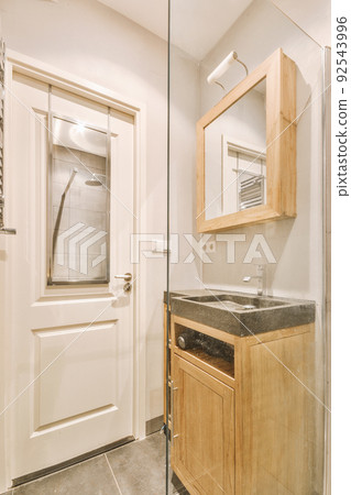 Cupboard with sink and mirror attached to tiled wall near door and drying rack in modern restroom 92543996