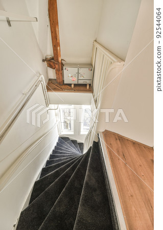 White spiral stairway connecting levels of contemporary house with wooden floor and white walls 92544064