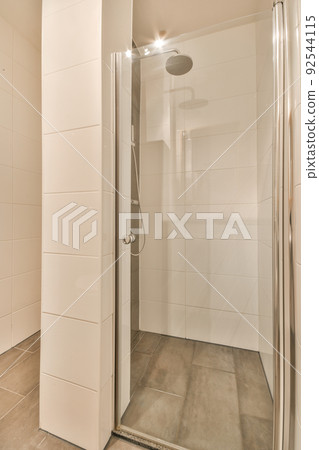 Shower faucets attached to tiled wall near glass partition and ornamental curtail in washroom at home Shower faucets attached to tiled wall near glass partition and ornamental curtail in washroom at home 92544115