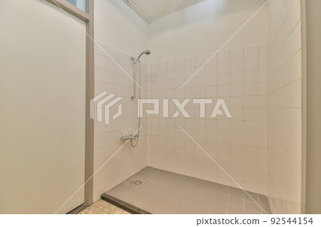 Shower faucets attached to tiled wall near glass partition and ornamental curtail in washroom at home 92544154