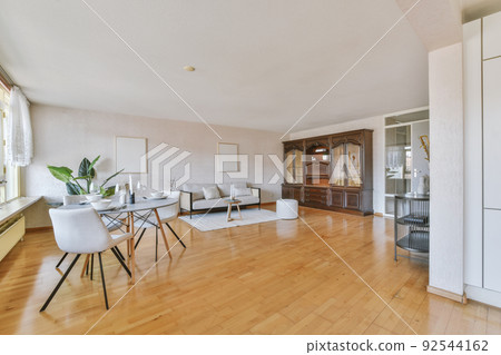 Stylish interior design of living room with light furniture and soft comfy couch and carpet in modern apartment with open kitchen and white walls Stylish interior design of living room with light furniture and soft comfy couch and carpet in modern apartment with open kitchen and white walls 92544162