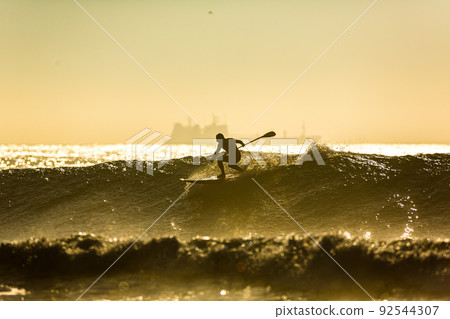 An unidentified surfer rides a big wave with foam at sunset An unidentified surfer rides a big wave with foam at sunset 92544307
