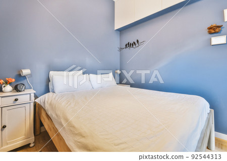 Minimalist interior design of small bedroom with soft bed placed in corner and wooden wardrobe and shelves with lamp illumination 92544313