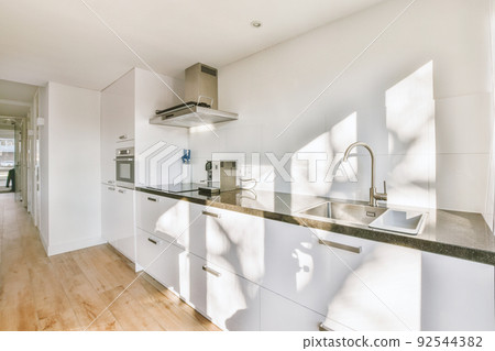 Interior of spacious light kitchen with modern white furniture and pop art portrait in light apartment Interior of spacious light kitchen with modern white furniture and pop art portrait in light apartment 92544382