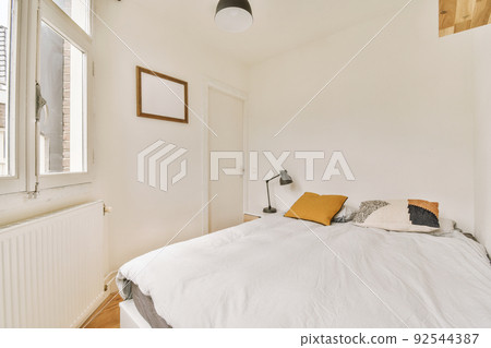 Minimalist interior design of small bedroom with soft bed placed in corner and wooden wardrobe and shelves with lamp illumination 92544387