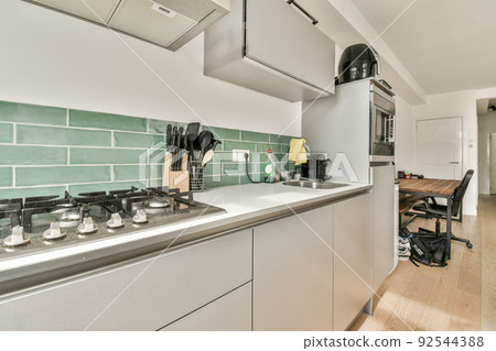 Simple open plan kitchen with white cabinets and living room with gray sofa in daylight 92544388