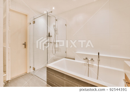 Sinks with mirrors and clean bathtub located near shower box with glass door in modern bathroom with white tiled walls 92544391