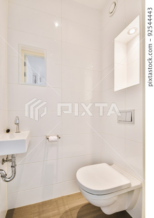 Wall hung toilet and small sink in corner in lavatory room with beige tile 92544443