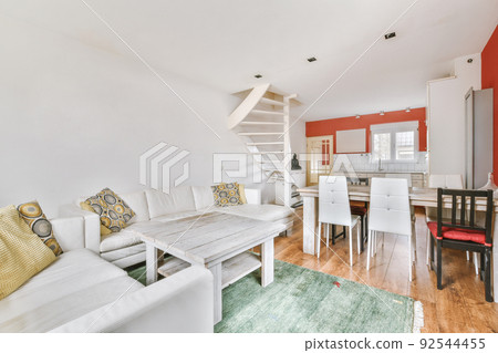 Cozy interior design of living room furnished with comfortable couch and wooden table decorated with carpet and lamp in modern attic apartment with white walls and column Cozy interior design of living room furnished with comfortable couch and wooden table decorated with carpet and lamp in modern attic apartment with white walls and column 92544455