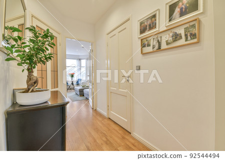 Interior of narrow corridor with many doors and classic painting on white walls 92544494