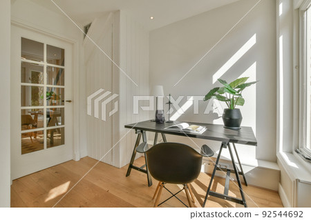 Modern minimalist style interior design of studio apartment with open white kitchen and dining zone with table and chairs illuminated by loft style lamp Modern minimalist style interior design of studio apartment with open white kitchen and dining zone with table and chairs illuminated by loft style lamp 92544692