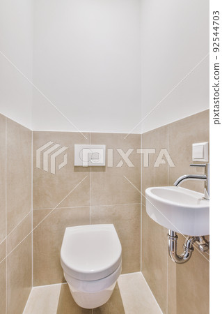 Interior of narrow restroom with sink and wall hung toilet with white walls and checkered floor 92544703