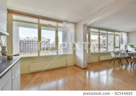 Stylish interior design of living room with light furniture and soft comfy couch and carpet in modern apartment with open kitchen and white walls Stylish interior design of living room with light furniture and soft comfy couch and carpet in modern apartment with open kitchen and white walls 92544885