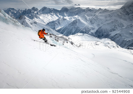Off-piste skier on a glacier going down a beautiful alpine landscape. Blue cloudy sky in the background and high mountains. Free space for text Off-piste skier on a glacier going down a beautiful alpine landscape. Blue cloudy sky in the background and high mountains. Free space for text 92544908