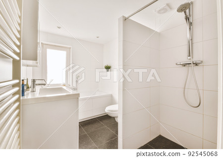 Modern flush toilet and ceramic sink installed on white tiled walls near mirror and towel in small restroom at home 92545068