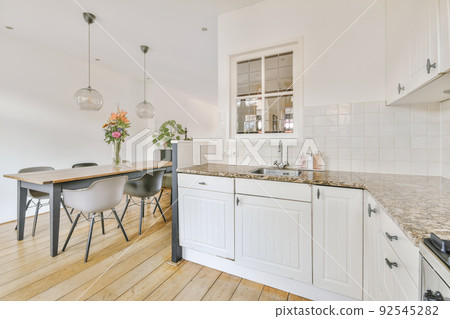 Wooden dining table under pendant lamp in open plan kitchen with living room 92545282