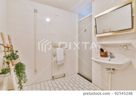 Cupboard with sink and mirror attached to tiled wall near door and drying rack in modern restroom 92545286