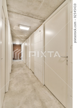 Light narrow hallway with many doors in white walls and glowing lamp over lumber floor 92545410