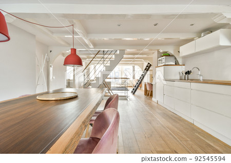 Contemporary cupboards with appliances and tables with kitchenware located in light kitchen near dining room in stylish apartment 92545594