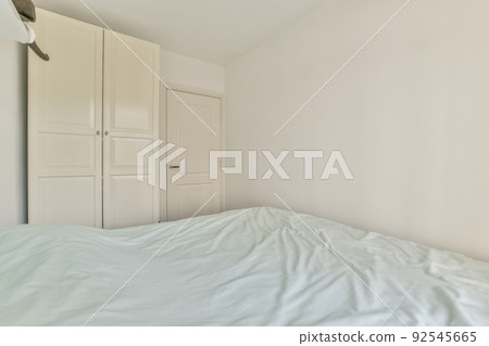 Home interior design of bedroom with bed and wooden wardrobe placed in corner near window in modern apartment Home interior design of bedroom with bed and wooden wardrobe placed in corner near window in modern apartment 92545665