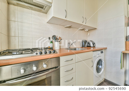 Fragment of interior of light narrow home kitchen with minimalist style white furniture with sink and stove 92545690