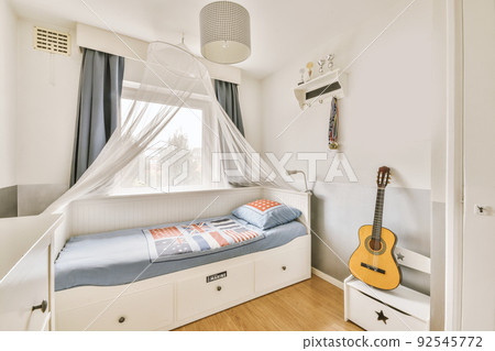 Comfortable bed with blanket and pillows located near closet and bedside table with lamp against window in small bedroom Comfortable bed with blanket and pillows located near closet and bedside table with lamp against window in small bedroom 92545772