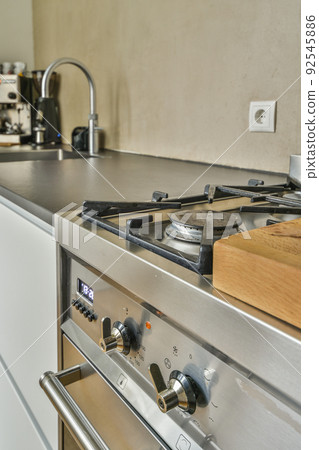 Fragment of interior of light narrow home kitchen with minimalist style white furniture with sink and stove Fragment of interior of light narrow home kitchen with minimalist style white furniture with sink and stove 92545886