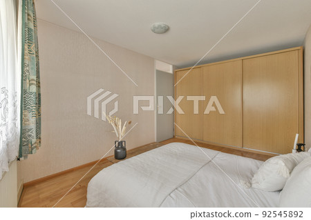 Home interior design of bedroom with bed and wooden wardrobe placed in corner near window in modern apartment 92545892