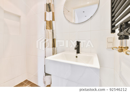 Cupboard with sink and mirror attached to tiled wall near door and drying rack in modern restroom 92546212