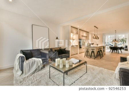Table with chairs and flowers located near lounge area and kitchen in spacious room of contemporary apartment Table with chairs and flowers located near lounge area and kitchen in spacious room of contemporary apartment 92546253