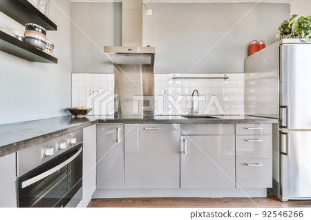 Modern home kitchen corner interior design with white cupboards and cabinets and steel hood over stove in contemporary apartment 92546266