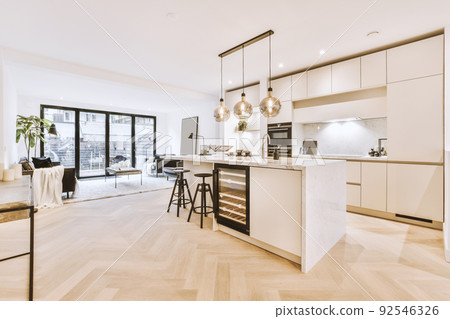 White cabinets with wooden counter of modern kitchen and dining table set in living room of apartment White cabinets with wooden counter of modern kitchen and dining table set in living room of apartment 92546326