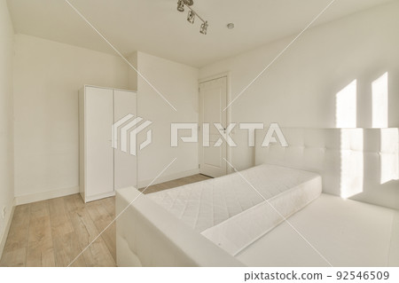 Minimalist interior design of small bedroom with soft bed placed in corner and wooden wardrobe and shelves with lamp illumination 92546509