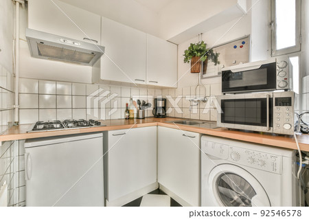 Fragment of interior of light narrow home kitchen with minimalist style white furniture with sink and stove Fragment of interior of light narrow home kitchen with minimalist style white furniture with sink and stove 92546578