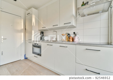 Modern home kitchen corner interior design with white cupboards and cabinets and steel hood over stove in contemporary apartment Modern home kitchen corner interior design with white cupboards and cabinets and steel hood over stove in contemporary apartment 92546912