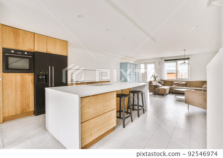 Contemporary open plan kitchen with dining table set and gray sofa in light spacious room 92546974