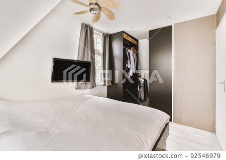 Minimalist interior design of small bedroom with soft bed placed in corner and wooden wardrobe and shelves with lamp illumination Minimalist interior design of small bedroom with soft bed placed in corner and wooden wardrobe and shelves with lamp illumination 92546979
