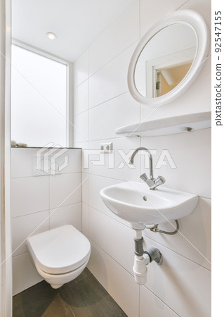 Interior of narrow restroom with sink and wall hung toilet with white walls and checkered floor Interior of narrow restroom with sink and wall hung toilet with white walls and checkered floor 92547155