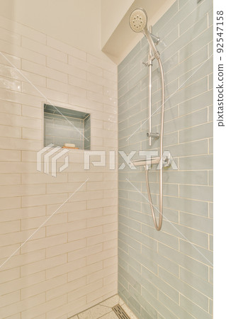 Shower faucets attached to tiled wall near glass partition and ornamental curtail in washroom at home Shower faucets attached to tiled wall near glass partition and ornamental curtail in washroom at home 92547158