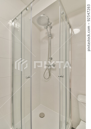 Tiled shower cabin with glass door located near sink and mirror in light restroom in contemporary apartment Tiled shower cabin with glass door located near sink and mirror in light restroom in contemporary apartment 92547263