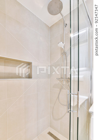 Shower faucets attached to tiled wall near glass partition and ornamental curtail in washroom at home 92547347