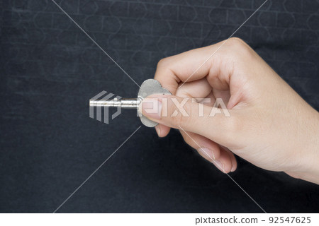 Woman hand holding key making door opening motion on black background Woman hand holding key making door opening motion on black background 92547625