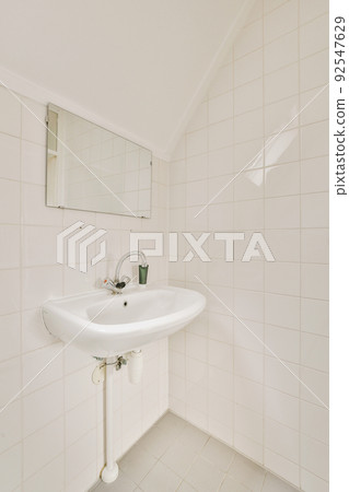 Bathtub with glass shower placed in corner near sink and mirror in small light bathroom with white tile walls Bathtub with glass shower placed in corner near sink and mirror in small light bathroom with white tile walls 92547629